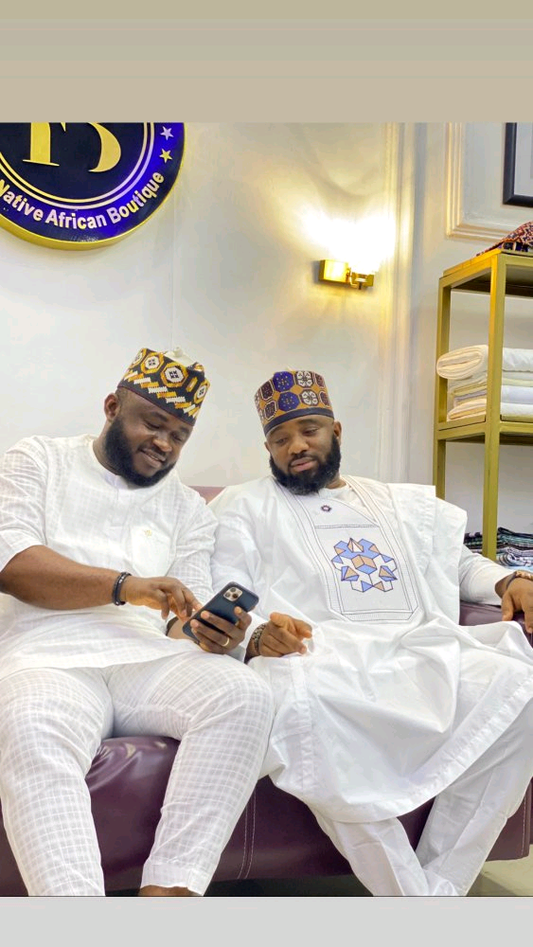 Man wearing a white embroidered Agbada set with geometric blue and gold detailing